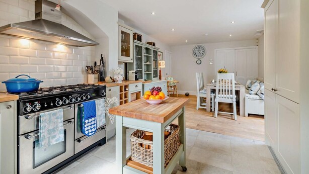 A modern kitchen with a stove, oven, and cabinets. There is a dining table with chairs and a clock on the wall. - 5 Bed in West Runton (oc-f27744) (West Runton)