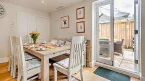 A dining area with a wooden table, white chairs, and a view of the backyard through a sliding glass door. - 5 Bed in West Runton (oc-f27744) (West Runton)