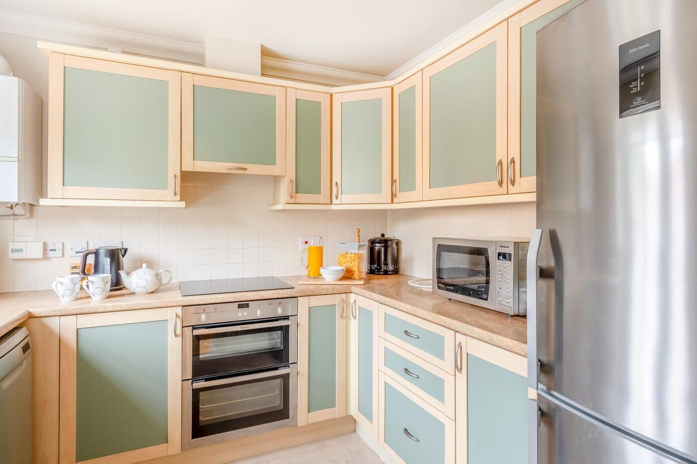 A kitchen with light green cabinets, a stainless steel refrigerator, a microwave, an oven, and a coffee maker.