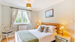 A bedroom with a bed, bedside lamps, a chair, a window with curtains, a radiator, and a painting on the wall. - 3 Bed in Wrentham (oc-m6144) (Wrentham)