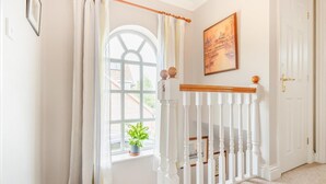 A staircase with a white railing, a window with a view of buildings, and a door with a golden handle. - 3 Bed in Wrentham (oc-m6144) (Wrentham)