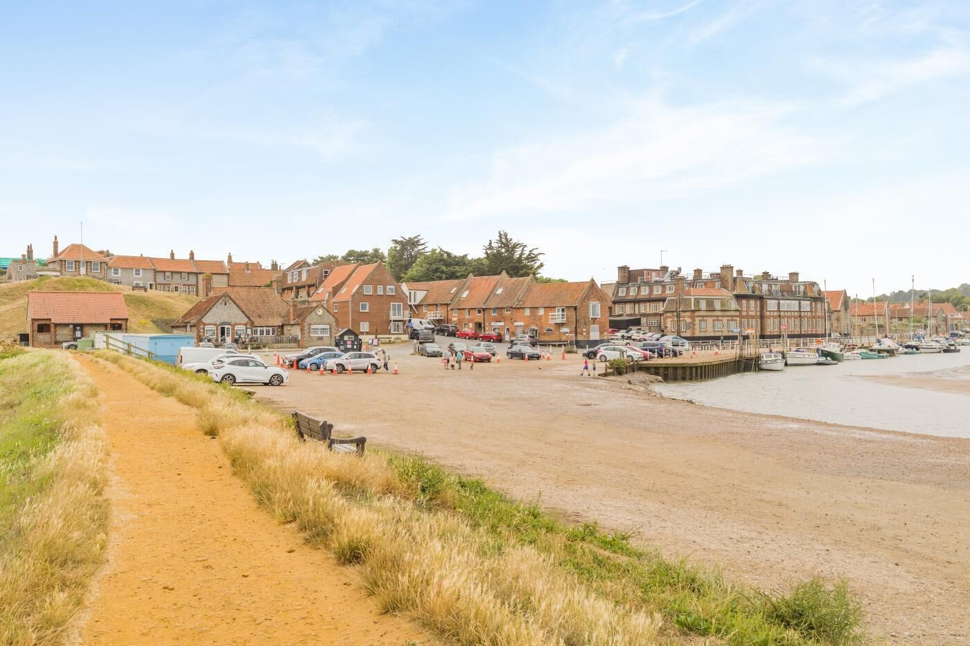 A coastal road leading to a sandy beach with parked cars and a row of houses.