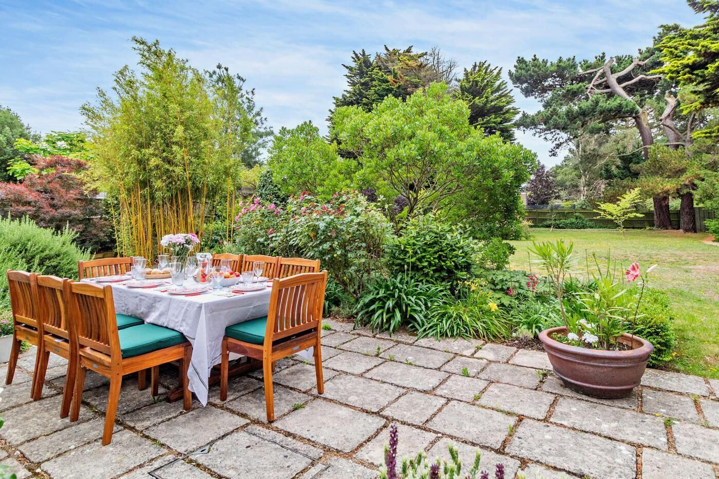 Een tuinpati met een eettafel, omringd door weelderige begroeiing en potplanten.