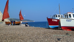 Une plage de galets où sont amarrés deux voiliers, l’un portant le numéro E282 et l’autre le numéro E127, près du rivage.