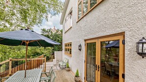 Une terrasse avec des meubles en bois, un parasol vert et une petite plante en pot.