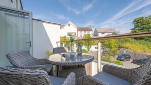 A balcony with wicker furniture, a glass table, and a view of the street and buildings. - 1 Bed in Saundersfoot (oc-pw927a) (Saundersfoot)