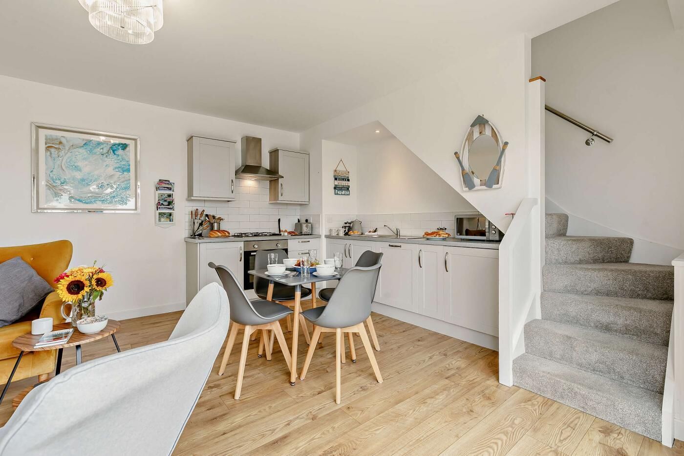 A modern kitchen with white cabinets, a dining area with grey chairs, and a staircase leading to another level.