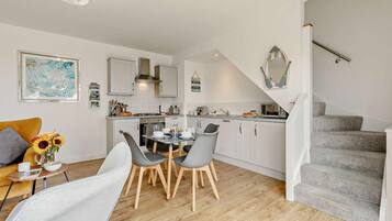 A modern kitchen with white cabinets, a dining area with grey chairs, and a staircase leading to another level.