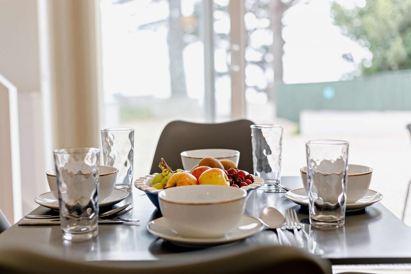 A dining table set with clear glassware, plates, and a bowl of fruit.