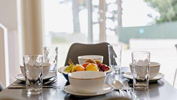 A dining table set with clear glassware, plates, and a bowl of fruit.