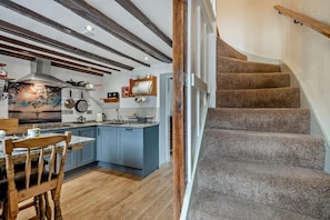 A kitchen with blue cabinets, a wooden dining table, and a staircase with carpeted steps. - 2 Bed in Bodham (oc-t27775) (Bodham)