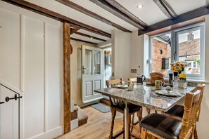 A kitchen with a granite countertop, wooden chairs, and a window with a view of a brick building. - 2 Bed in Bodham (oc-t27775) (Bodham)