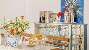 Une table à manger avec un vase de fleurs, une théière et une assiette contenant un sandwich.