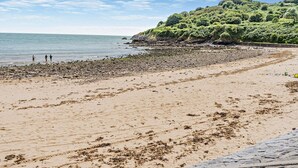 Une plage bordée d’une côte rocheuse, avec une colline boisée en arrière-plan.