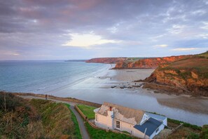 A coastal landscape with a beach, cliffs, and a house with a pathway leading to it. - 3 Bed in Broad Haven (oc-w27772) (Broad Haven)