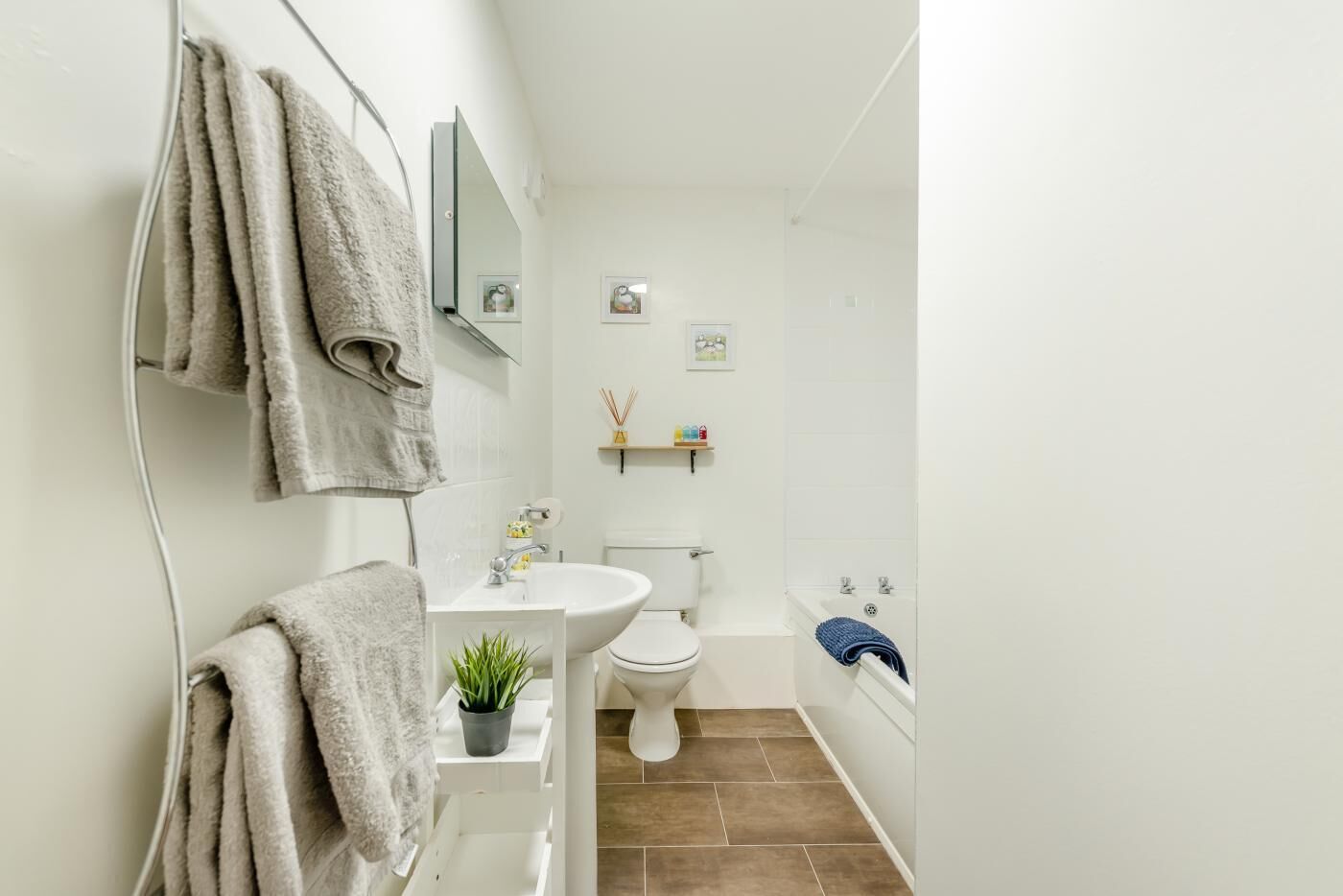 A bathroom with a sink, toilet, and bathtub. There are towels hanging on a rack, a potted plant on the sink, and a mirror above the sink.
