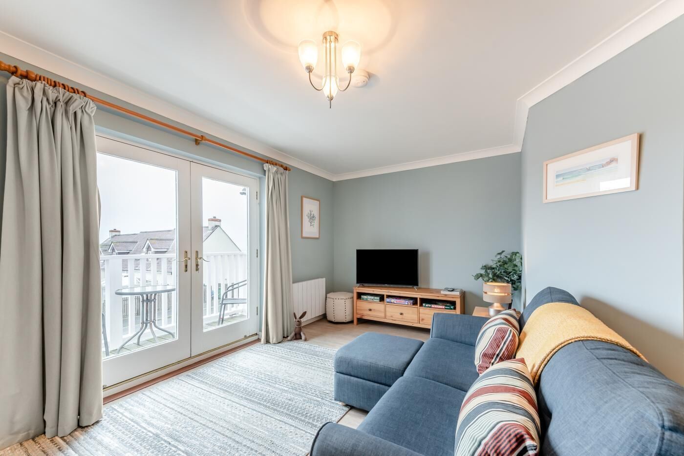 Un salon avec un canapé, un téléviseur et une vue sur l’extérieur, accessible par une porte-fenêtre coulissante.