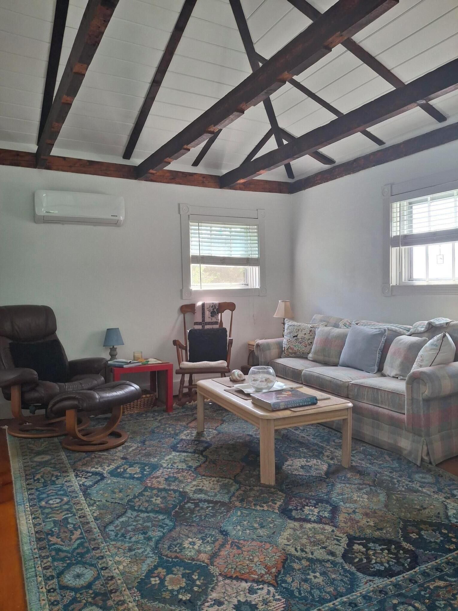 A living room with a sofa, a chair, a coffee table, a rug, and a window with blinds.