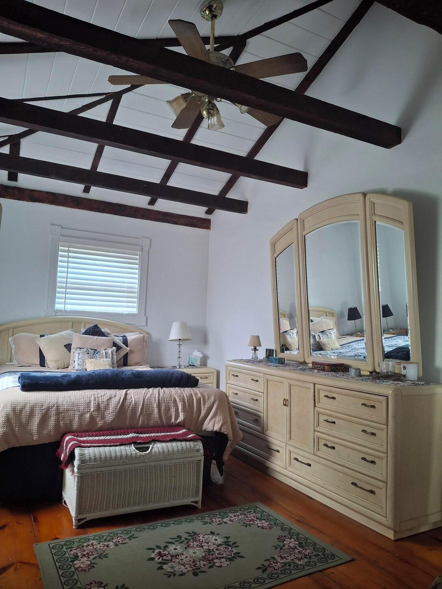 A bedroom with a bed, dresser, mirror, and ceiling fan.