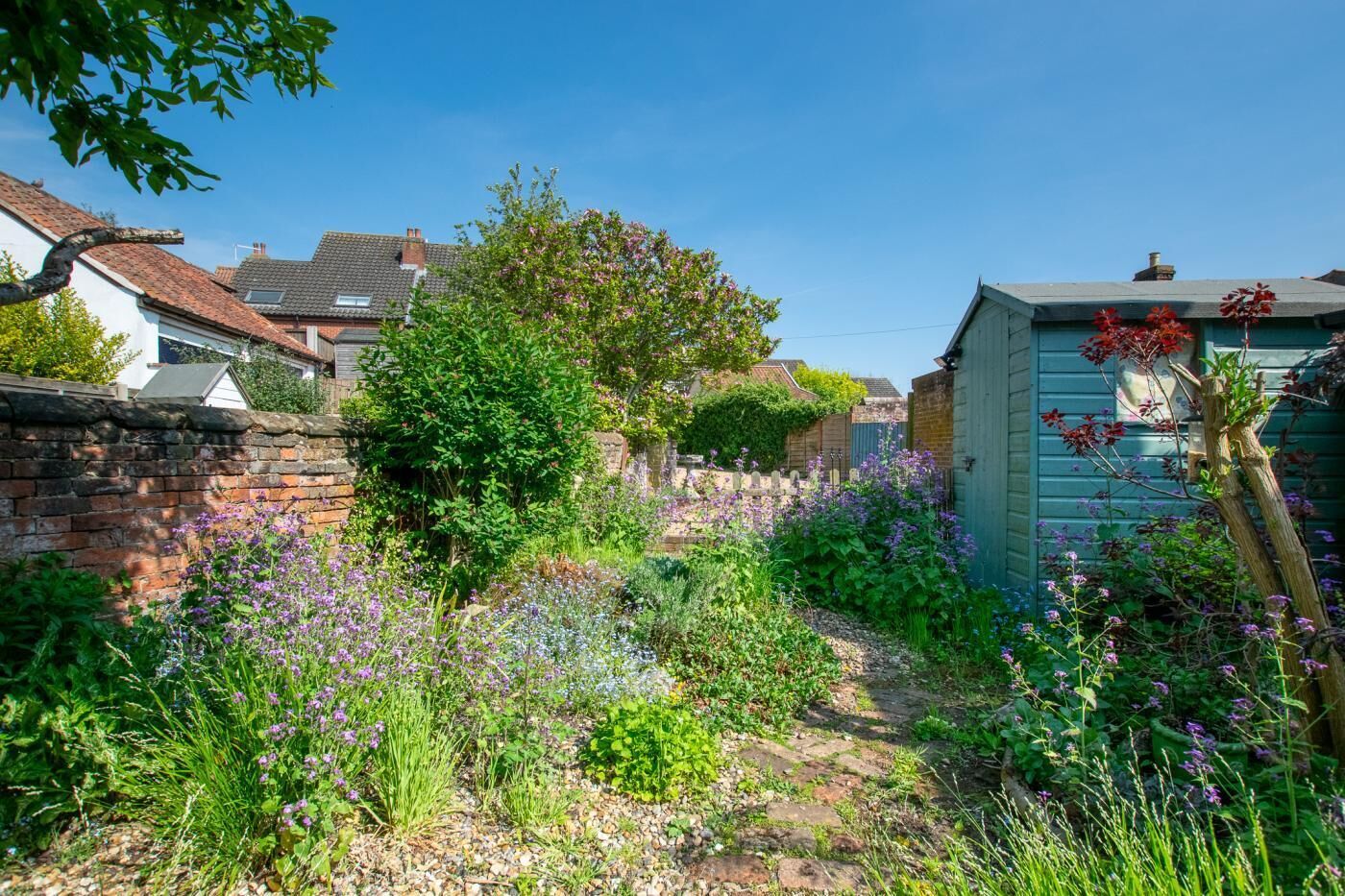 A garden with a brick wall, a wooden shed, and a house in the background.