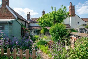 Ein traditionelles Cottage mit Garten, einem Holzzaun und einem Schild mit der Aufschrift 'MAN'S AGE'.