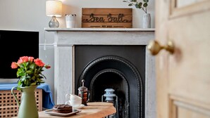 Une pièce chaleureuse avec une cheminée, une enseigne en bois au-dessus, une table ornée d’un vase de fleurs et une lampe.