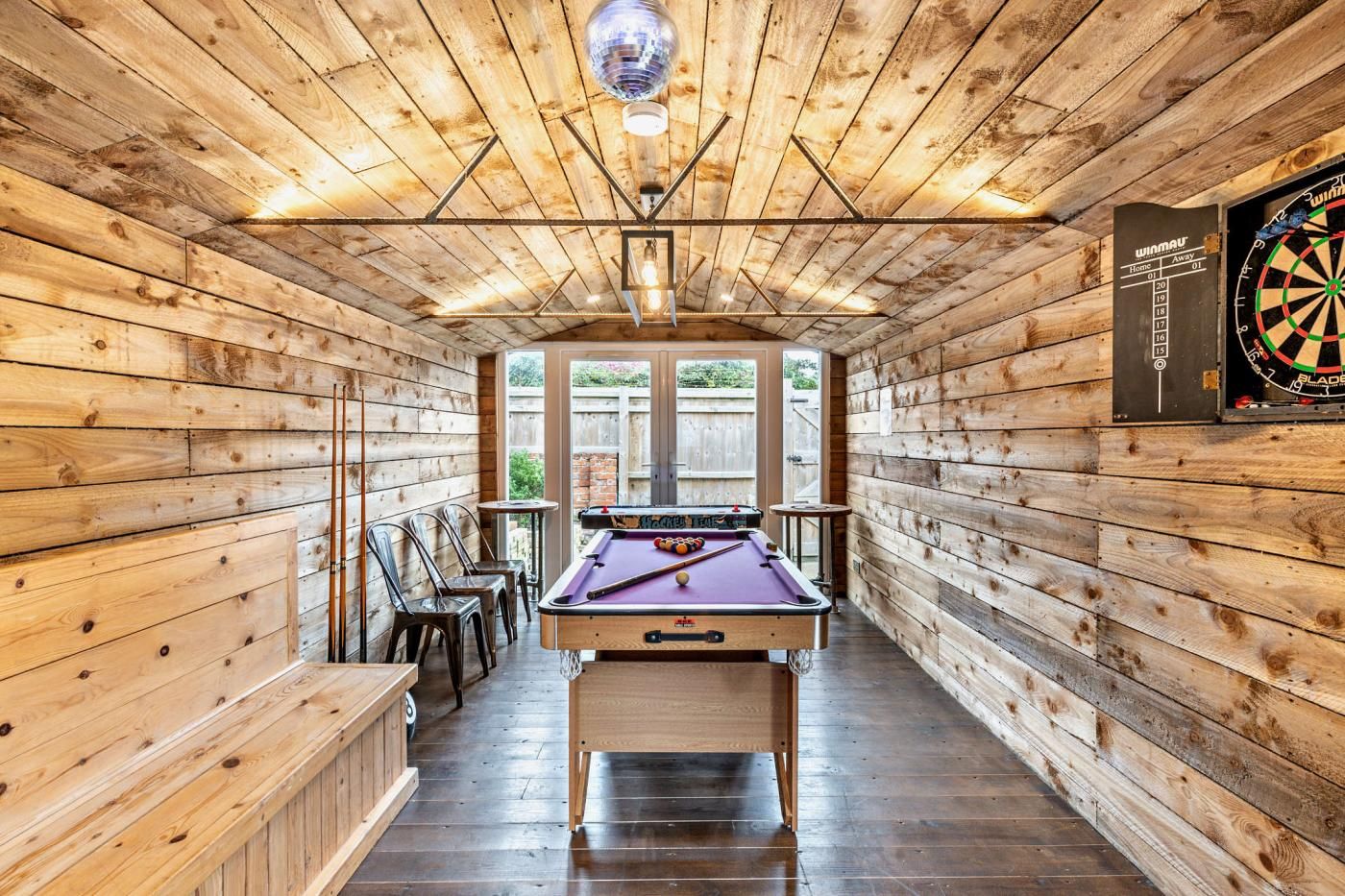 Un tavolo da biliardo in una stanza in legno con un bersaglio da freccette appeso al muro.