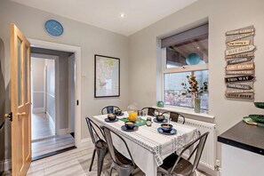 A dining area with a table set for four, a clock on the wall, and a window with a view. - 3 Bed in Felixstowe (oc-s27808) (Felixstowe)