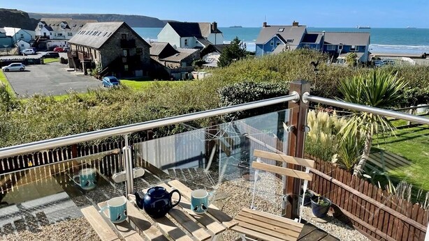 Una terrazza con ringhiera in vetro che si affaccia su una spiaggia e delle case.