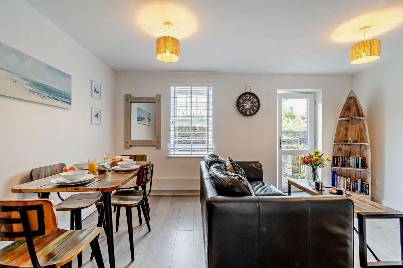 A modern living room with a dining area, featuring a leather sofa, wooden dining table, and a bookshelf.