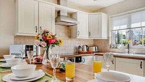 Una cocina moderna con armarios blancos, una campana extractora de acero inoxidable, una mesa de comedor preparada con platos, vasos y un florero.