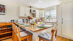 Una cocina moderna con armarios blancos, una mesa de comedor de madera y sillas. Hay una ventana que proporciona luz natural y vistas al exterior.