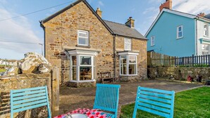 A stone house with a bay window, a small garden, and a table with a checkered tablecloth and chairs. - 4 Bed in Broad Haven (oc-t27866) (Broad Haven)