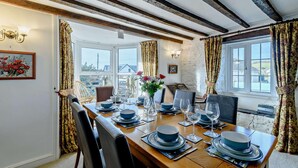 A dining room with a wooden table set for six, large windows, and a stone wall. - 4 Bed in Broad Haven (oc-t27866) (Broad Haven)