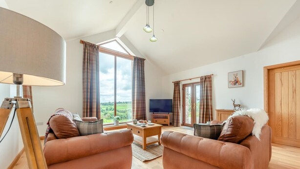 Ein gemütliches Wohnzimmer mit zwei Ledersofas, einem Holztisch, einem Fernseher und einem großen Fenster mit Vorhängen.