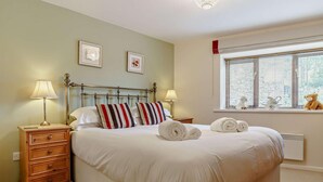 Ein ordentlich gemachtes Bett mit gestreiften Kissen, ein Nachttisch mit Lampen und ein Fenster mit Jalousien und Dekoration.
