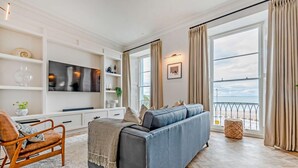 A modern living room with a sofa, TV, and large windows overlooking a balcony. - 2 Bed in Tenby (oc-s27901) (Tenby)