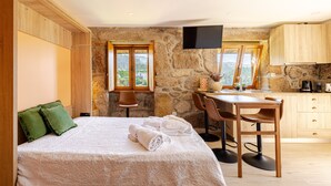 A room with a bed, a desk, a chair, a TV, and a stone wall.
