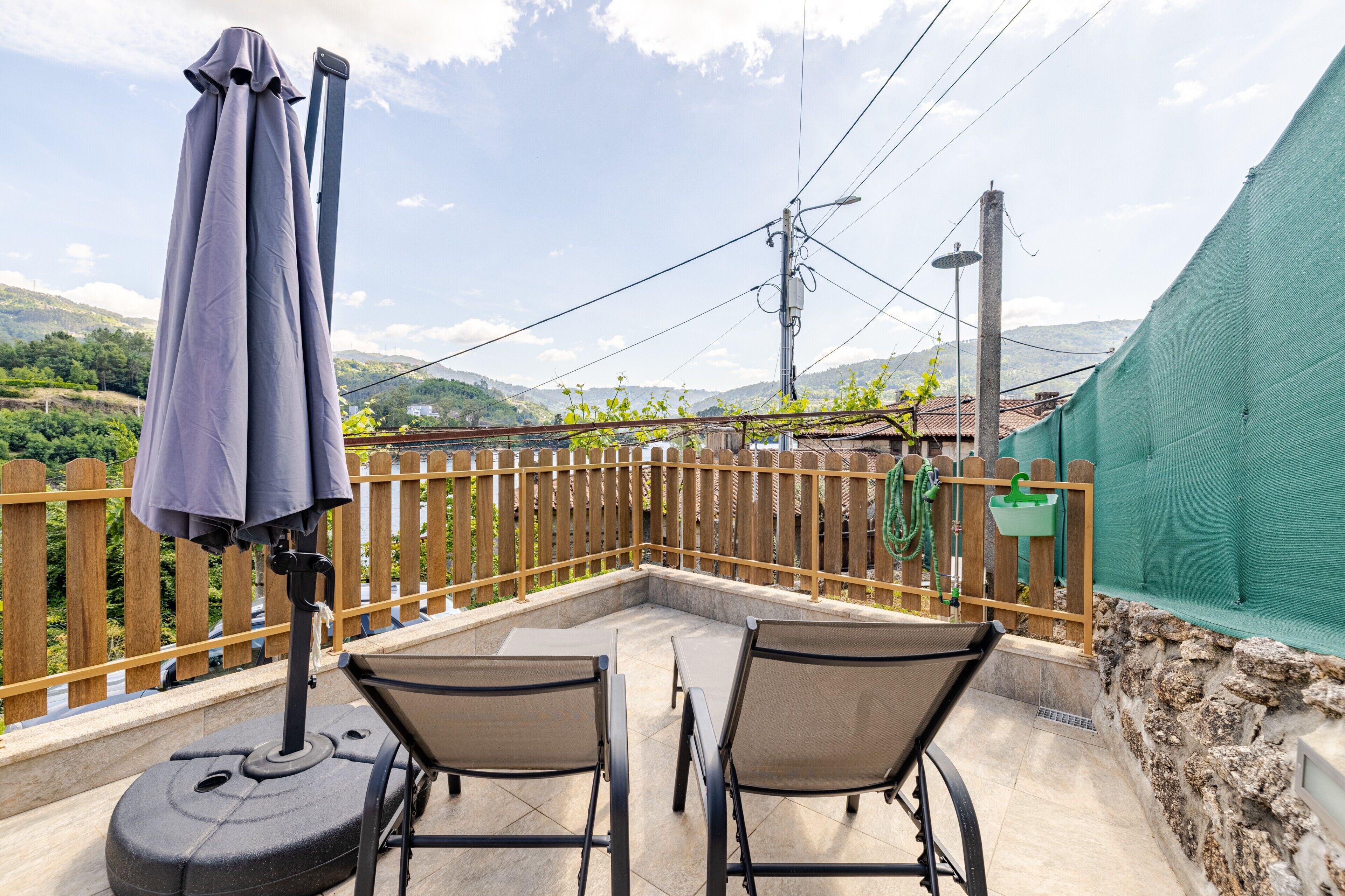 A patio with two chairs and a table, a wooden fence, and a view of hills.