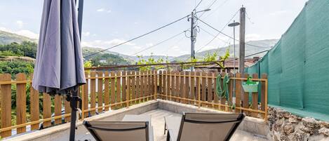 A patio with two chairs and a table, a wooden fence, and a view of hills.