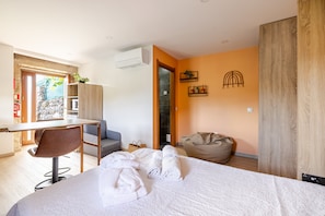 Une chambre d’hôtel moderne équipée d’un lit, d’un bureau, d’une chaise, d’un fauteuil poire et d’un petit balcon.