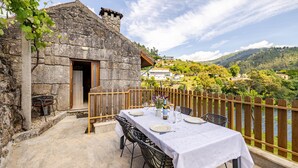 A stone building with a balcony overlooking a river, a table set for dining, and a view of the surrounding landscape.