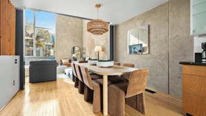 A modern kitchen with a dining area, wooden flooring, and a large window with a view of trees. - Gaslamp Row House - Sleeps 8, Private Garage, AC (San Diego)