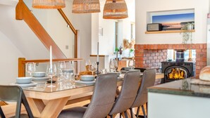 A dining area with a wooden table set for four, surrounded by chairs, and a brick fireplace in the background. - 4 Bed in Newquay (oc-b27906) (Newquay)