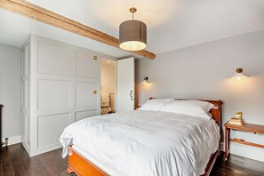 A bedroom with a large bed, wooden headboard, and a ceiling light fixture. - 3 Bed in Burton Bradstock (oc-t27822) (Burton Bradstock)