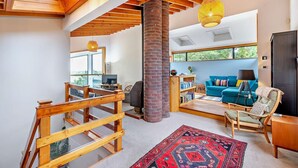 A spacious living area with a wooden staircase, a brick fireplace, a blue sofa, and a large window offering a view of greenery. - 5 Bed in Rye (oc-o27820) (Rye)