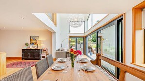 A dining area with a long table set for six, a chandelier, and a view of the outdoors through large windows. - 5 Bed in Rye (oc-o27820) (Rye)