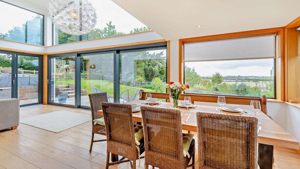 A dining area with wicker chairs, a wooden table, and a view of the garden through large windows. - 5 Bed in Rye (oc-o27820) (Rye)