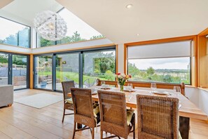 A dining area with wicker chairs, a wooden table, and a view of the garden through large windows. - 5 Bed in Rye (oc-o27820) (Rye)