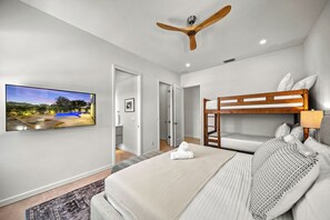 Ett modernt hotellrum med en stor TV, våningssängar, en takfläkt och utsikt över en pool.
